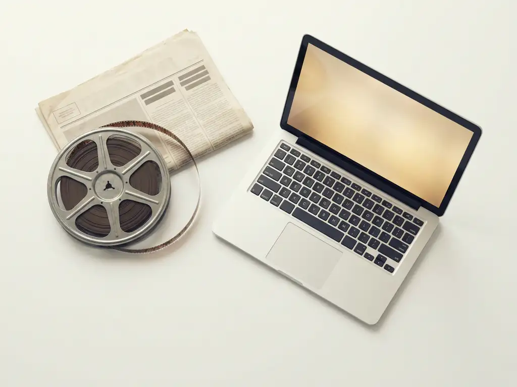 Vintage filmrol en gevouwen krant naast een open laptop op wit oppervlak, minimalistische flatlay in ivoor, houtskool en goud.